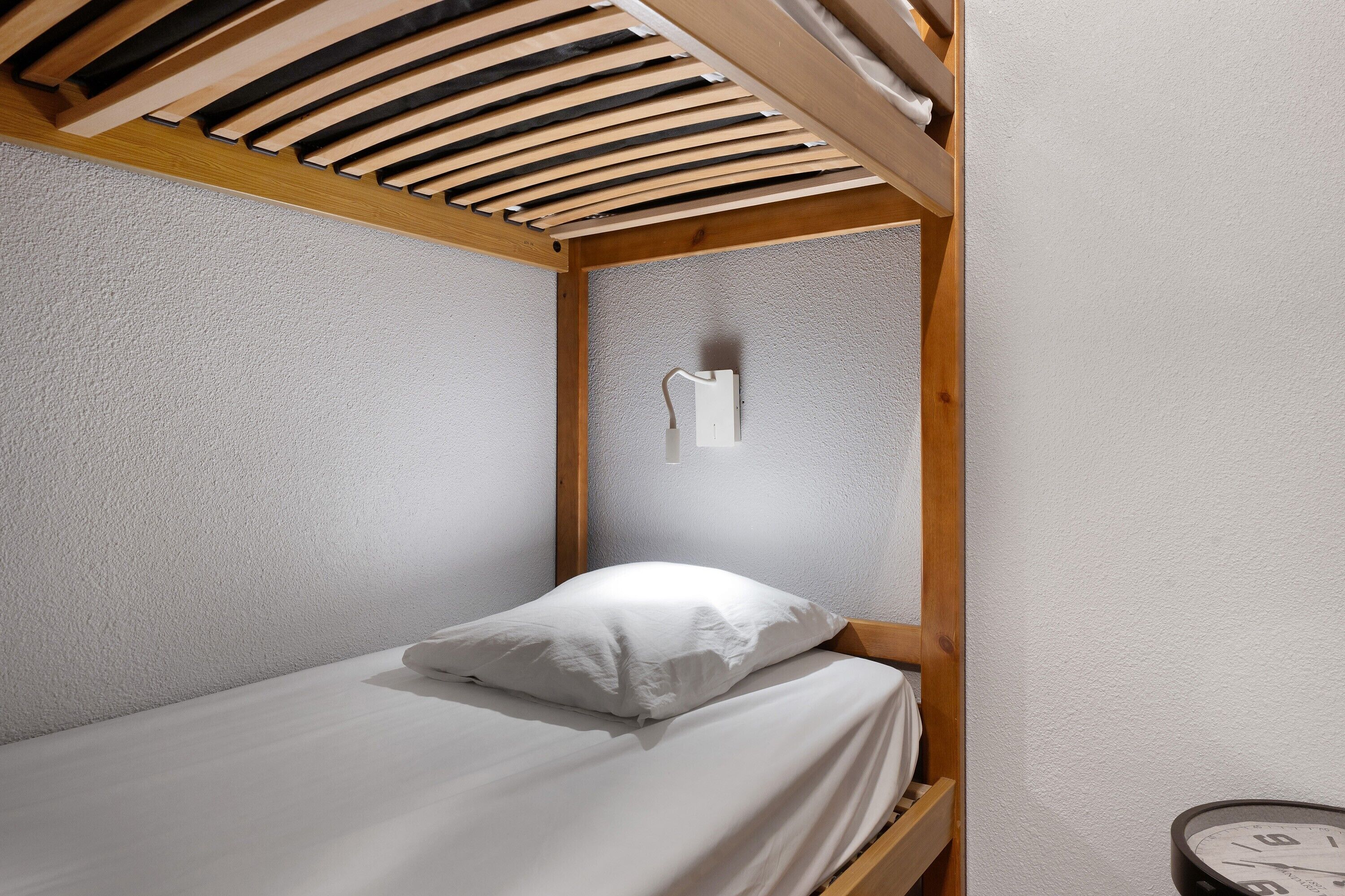 Ein Einzelbett mit weißer Matratze und Kissen in einem Zimmer mit strukturierter Wand und Holzbalken.