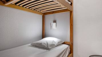 Ein Einzelbett mit weißer Matratze und Kissen in einem Zimmer mit strukturierter Wand und Holzbalken.