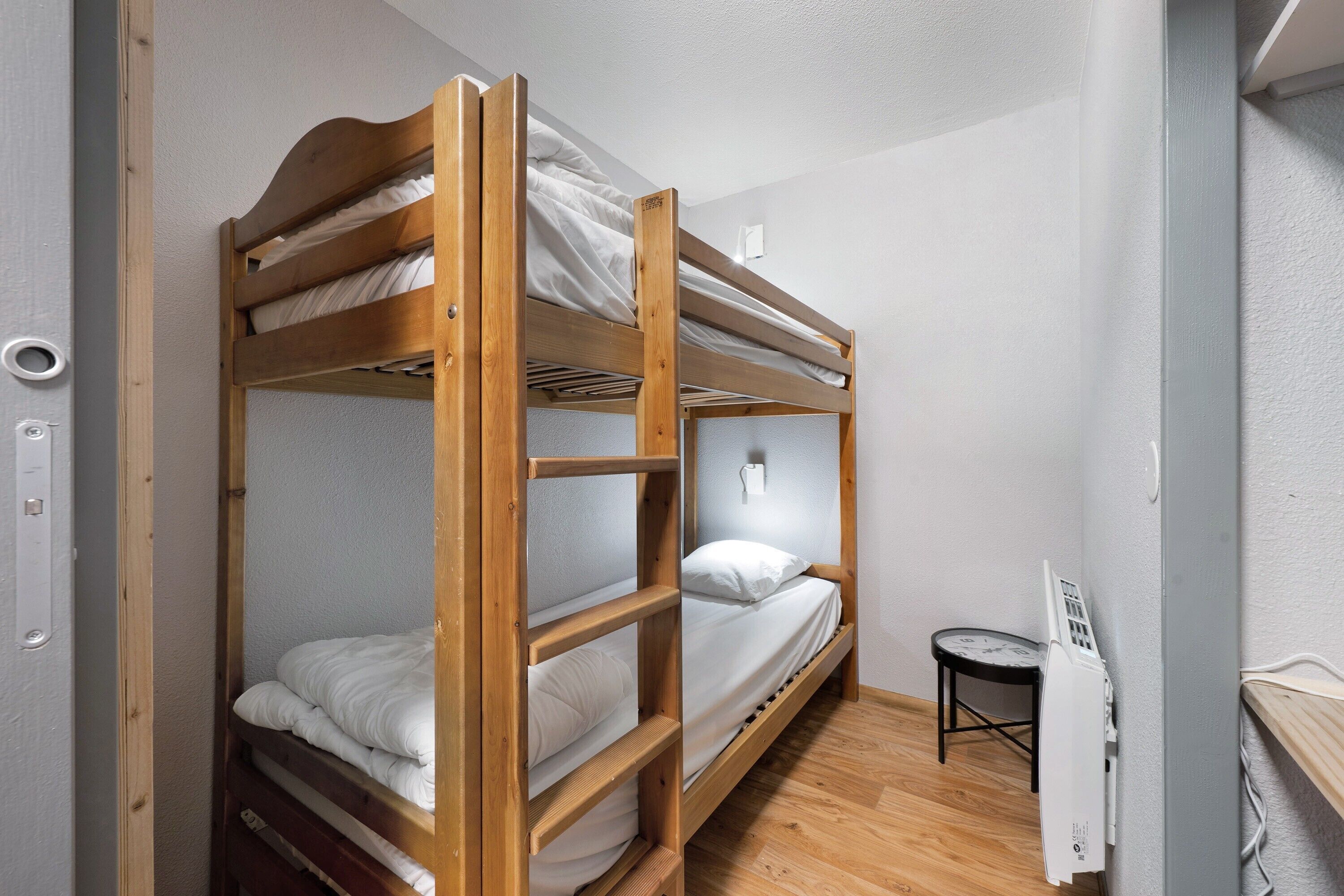 Une chambre avec un lit superposé en bois, une petite table et un radiateur fixé au mur.