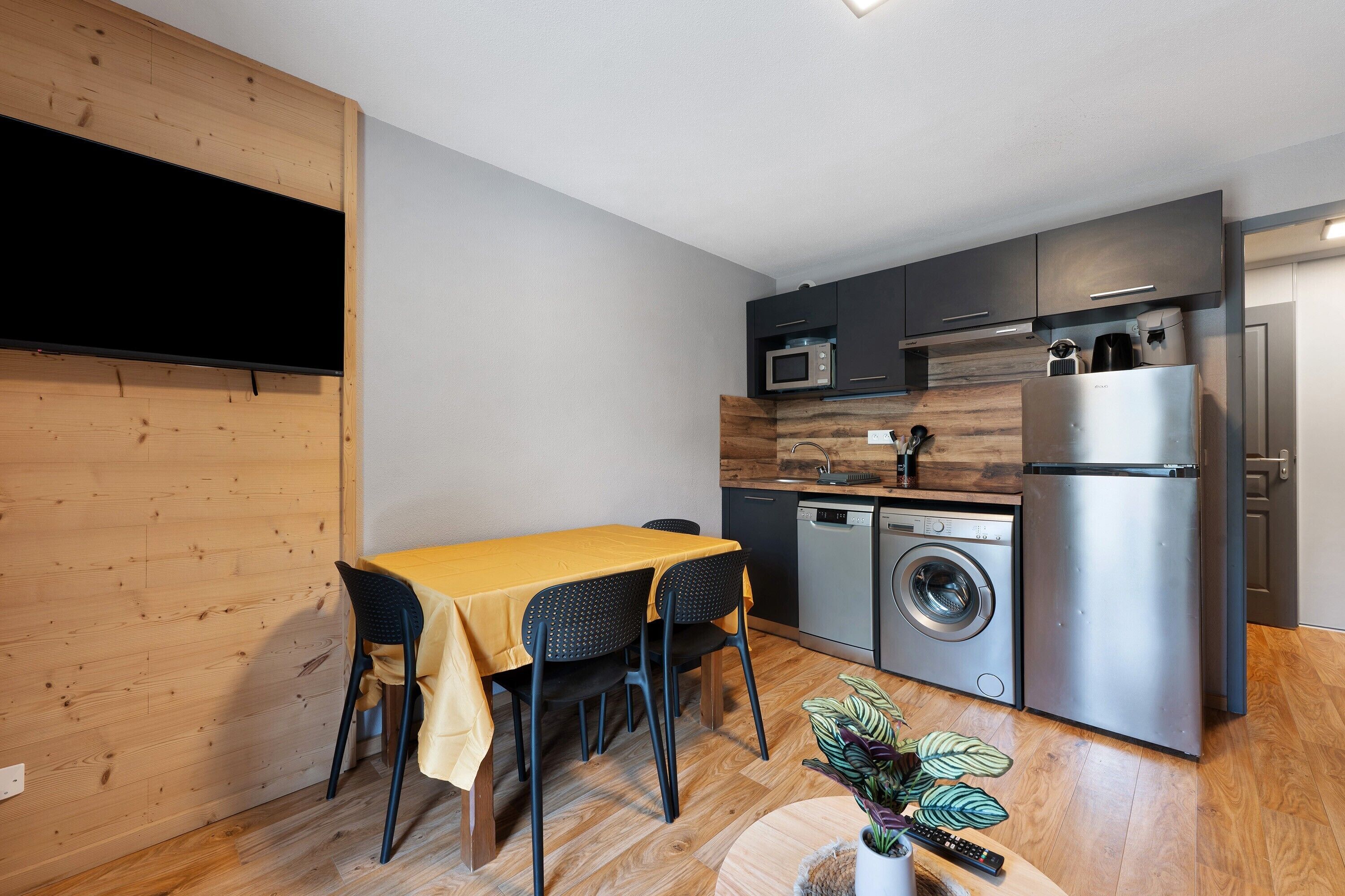 Een functionele keuken met een eethoek, inclusief een tafel met stoelen, een wasmachine, een koelkast en een magnetron.