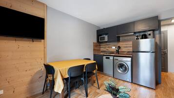 Een functionele keuken met een eethoek, inclusief een tafel met stoelen, een wasmachine, een koelkast en een magnetron.