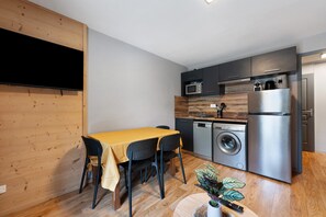 Uma cozinha compacta com área de jantar, incluindo uma mesa com cadeiras, máquina de lavar roupa, frigorífico e micro-ondas.