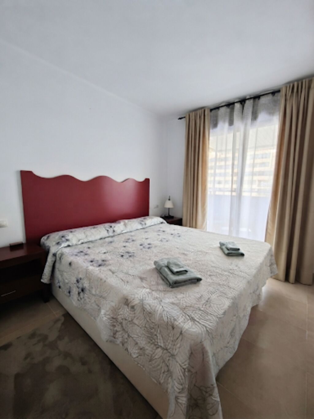 A hotel room with a bed, a nightstand, a lamp, and a window with curtains.