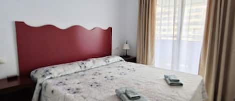 A hotel room with a bed, a nightstand, a lamp, and a window with curtains.