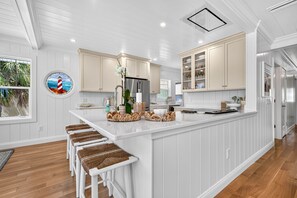 Een moderne keuken met witte kasten, een centraal eiland met krukken, en uitzicht op de omgeving door een raam.