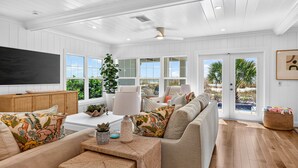 A spacious living room with a large flat-screen TV, comfortable seating, and a view through the glass doors. - Sandcastle Villa 3BR Beachfront Home (Clearwater Beach)