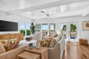 A spacious living room with a large flat-screen TV, comfortable seating, and a view through the glass doors. - Sandcastle Villa 3BR Beachfront Home (Clearwater Beach)