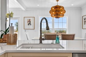 A modern kitchen with a stainless steel sink, a decorative chandelier, and a view of the outdoors through large windows. - Sandcastle Villa offered by Beach Time Rentals (Clearwater Beach)