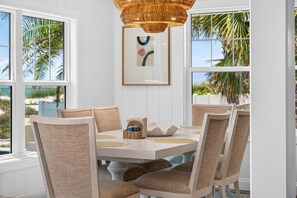 A dining area with a round table, six chairs, a woven light fixture, and a framed abstract artwork. - Sandcastle Villa offered by Beach Time Rentals (Clearwater Beach)