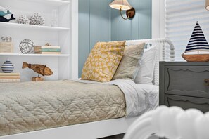 A bedroom with a bed, a nightstand, a lamp, and a shelf with decorative items. - Sandcastle Villa offered by Beach Time Rentals (Clearwater Beach)