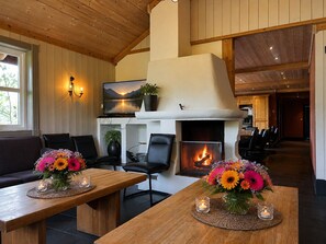 A cozy living room with a fireplace, wooden furniture, and a television mounted above it.