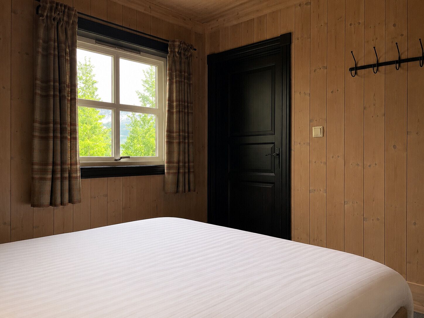 A room with a bed, a window with curtains, a door, and a coat rack.