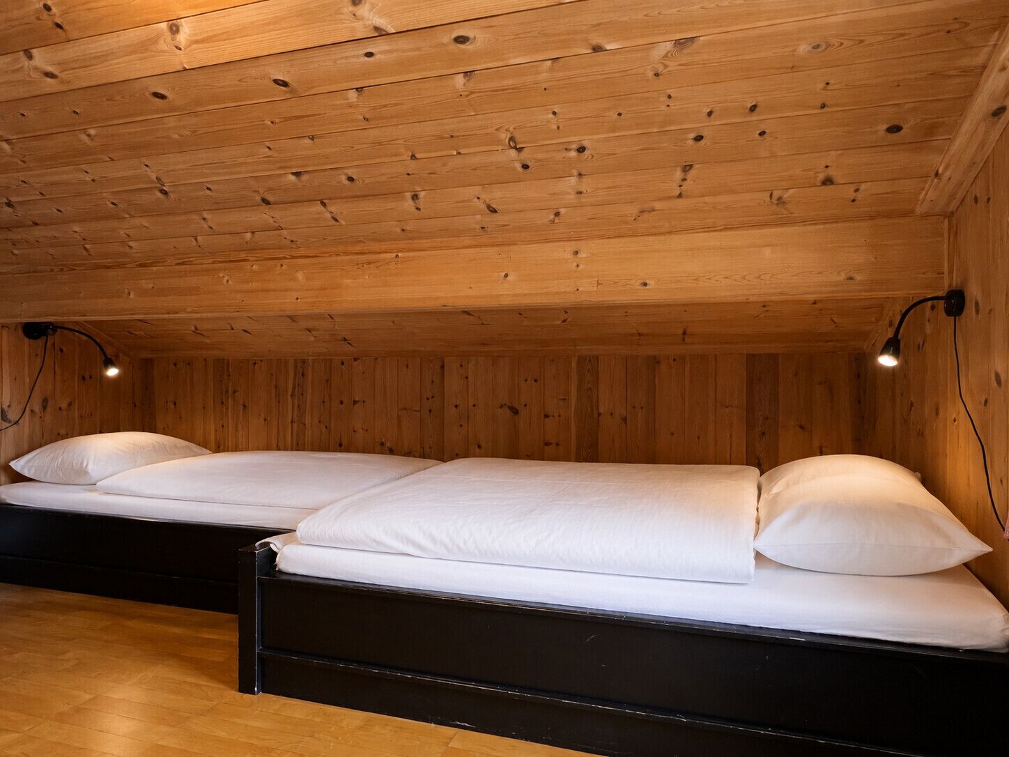 A room with two beds, wooden walls, and a sloped ceiling.