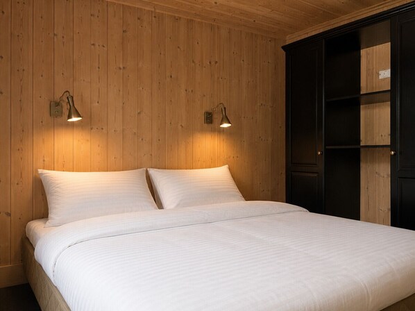 A bed with two pillows and two wall-mounted lamps in a room with wooden paneling.