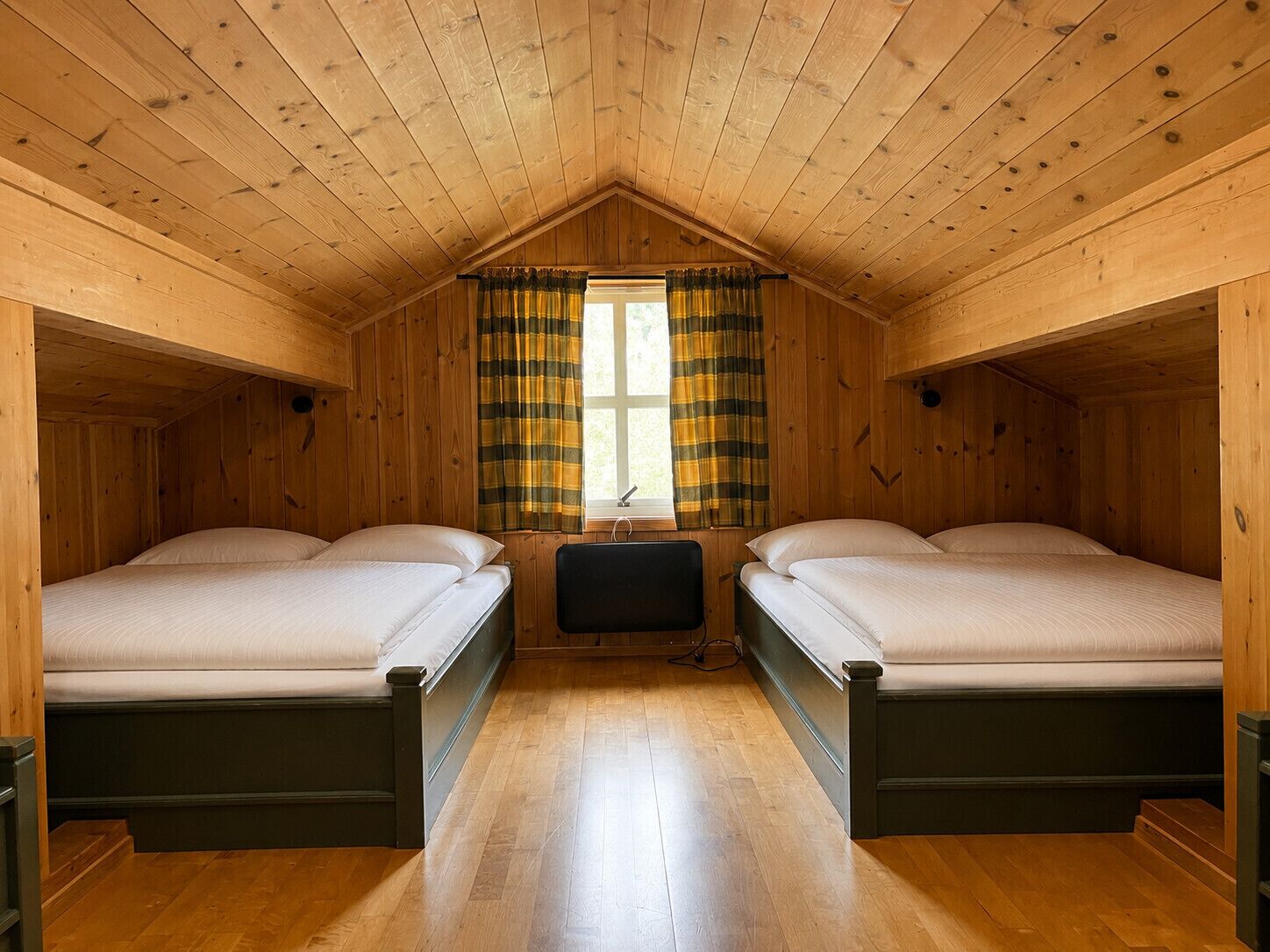 A cabin with two beds, a window with curtains, and wooden walls.