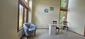 Ein Zimmer mit Schreibtisch, zwei Stühlen, einem gemusterten Sessel und zwei an der Wand befestigten Kunstwerken.