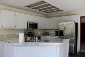 A kitchen with white cabinets, stainless steel appliances, a marble countertop, and a built-in oven. - The Johnston Paradise (Johnston)