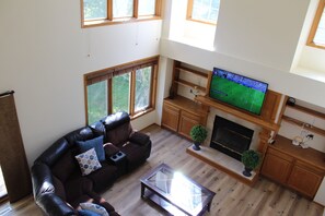 Ein Wohnzimmer mit einer Ledersofa, einem Glastisch, einem Kamin und einem Fernseher, der ein Fußballspiel zeigt.