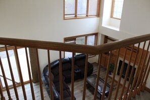 A staircase with wooden railings leading to a living area with a leather sofa and a fireplace. - The Johnston Paradise (Johnston)