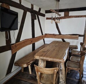 A rustic wooden table with benches, a television mounted on the wall, and exposed wooden beams. - LANDHAUS ELLENBACH - Romantic Half-Timbered Charm on the Fulda River, Cozy Vacation Rental in a Historic Building (Alheim)