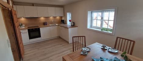 A compact kitchen with white cabinets, a wooden dining table set for four, and a window with a view of the outside.