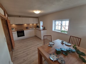 A compact kitchen with white cabinets, a wooden dining table set for four, and a window with a view of the outside. - LANDHAUS ELLENBACH - Romantic Half-Timbered Charm on the Fulda River, Cozy Vacation Rental in a Historic Building (Alheim)
