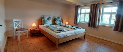 A bedroom with a wooden bed, two bedside lamps, a chair, and a window with curtains.