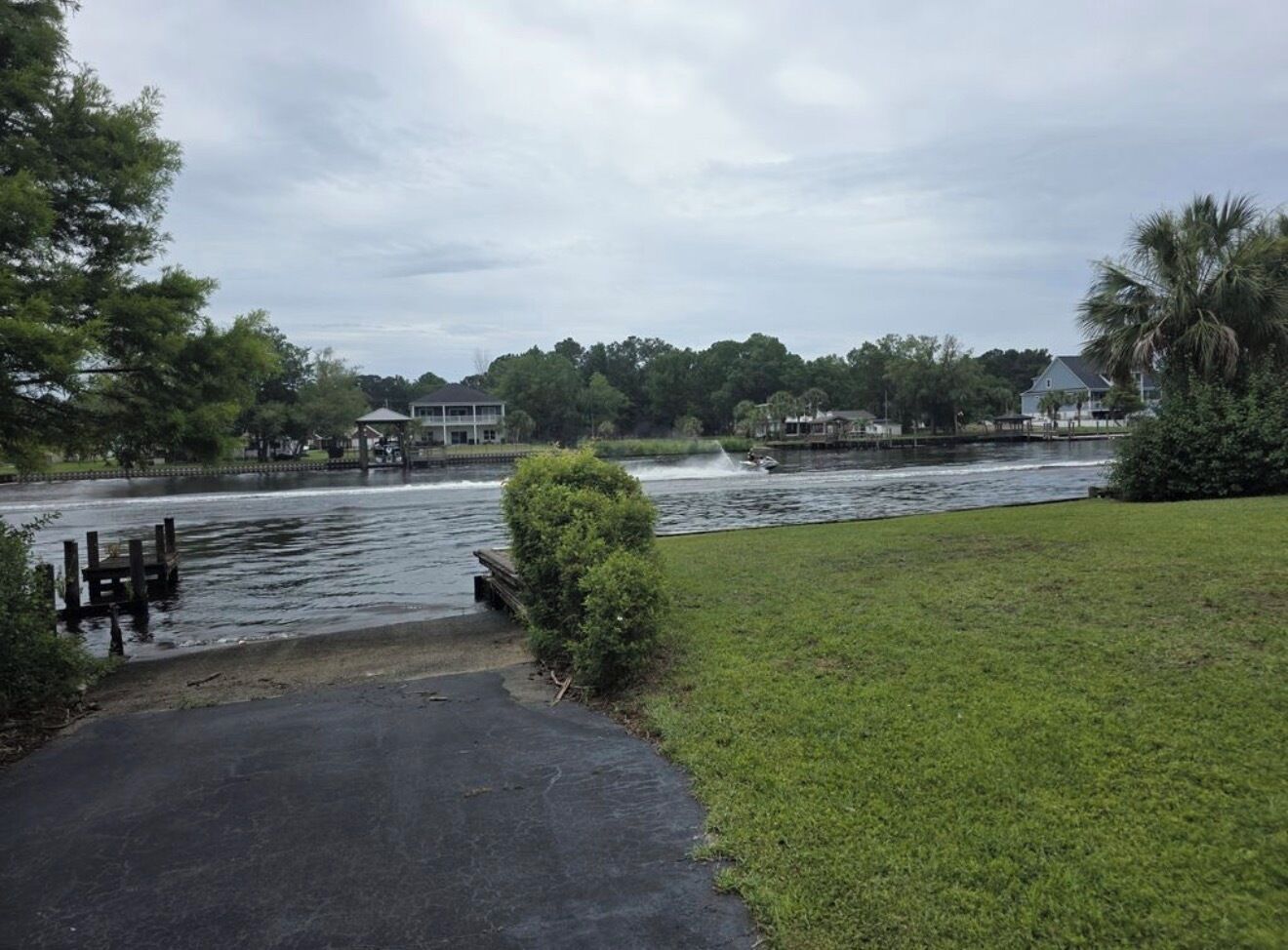 A riverside pathway with a grassy area, a dock, and a building in the background.