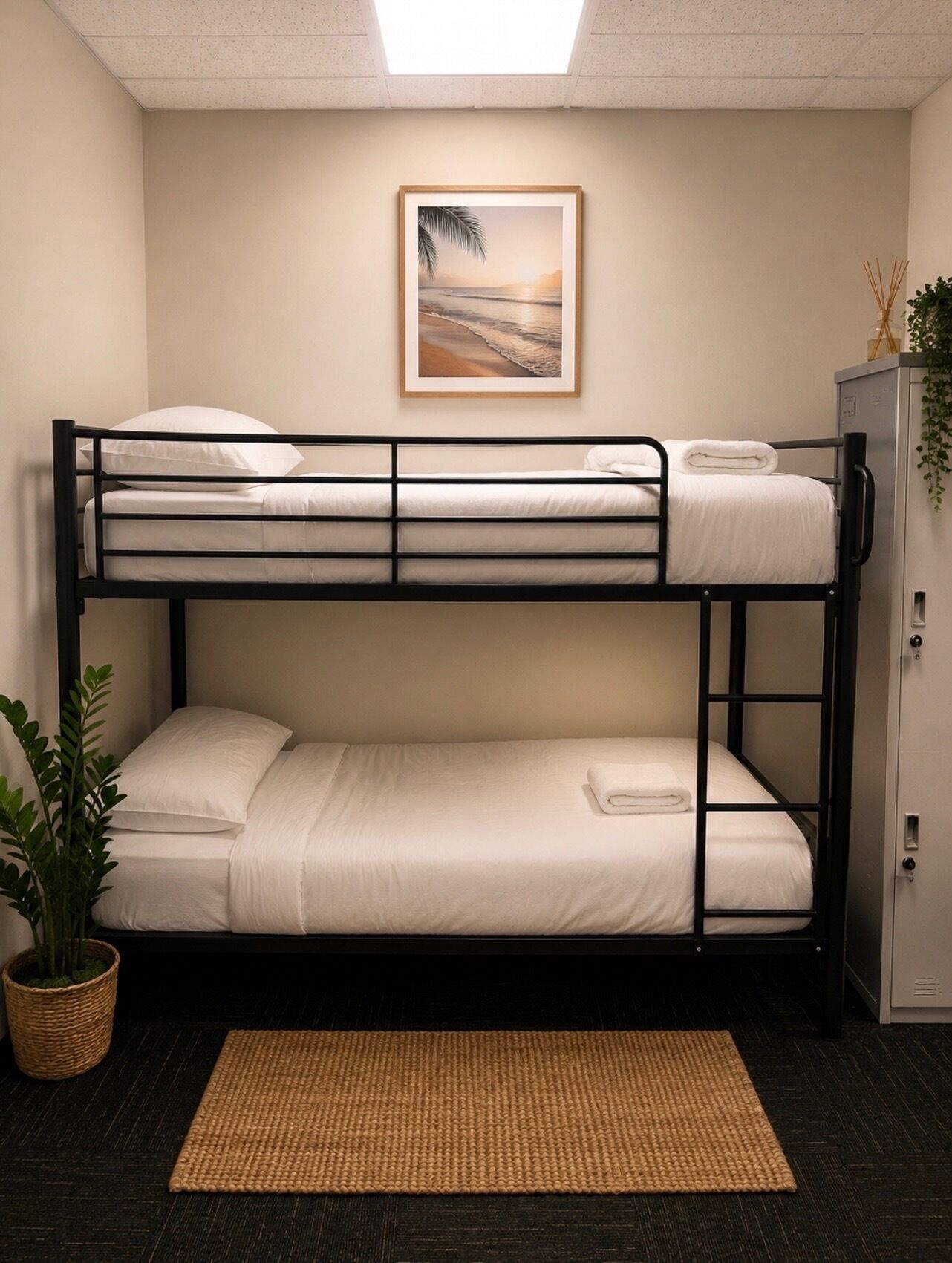 A bunk bed room with a framed picture on the wall, a small cabinet, and a woven mat on the floor.