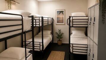 A bunk room with three bunk beds, a small potted plant, a framed picture on the wall, and a cabinet with a plant on top.