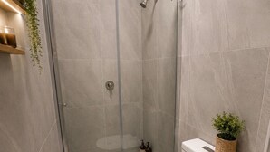 A modern bathroom with a glass-enclosed shower, a white toilet, and a small plant on the toilet tank. - Brunsi hostel (Brunswick)