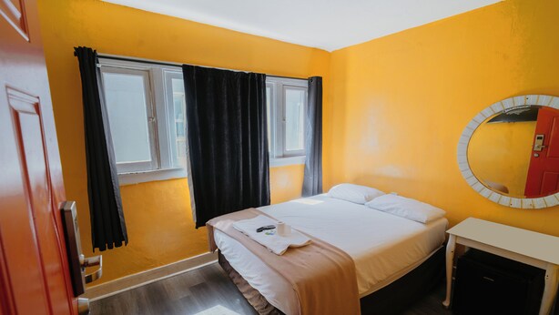 Habitación de hotel con cama, mesita de noche, espejo, ventana con cortinas y puerta.