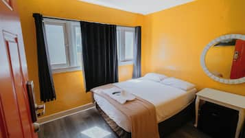Une chambre d’hôtel avec un lit, une table de chevet, un miroir, une fenêtre avec des rideaux et une porte.