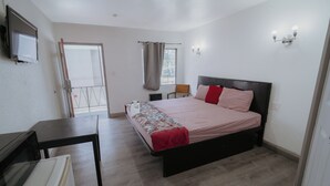 A bedroom with a bed, a desk, a chair, a television, and a window with curtains. - Clarendon Hotel (Huntington Park)