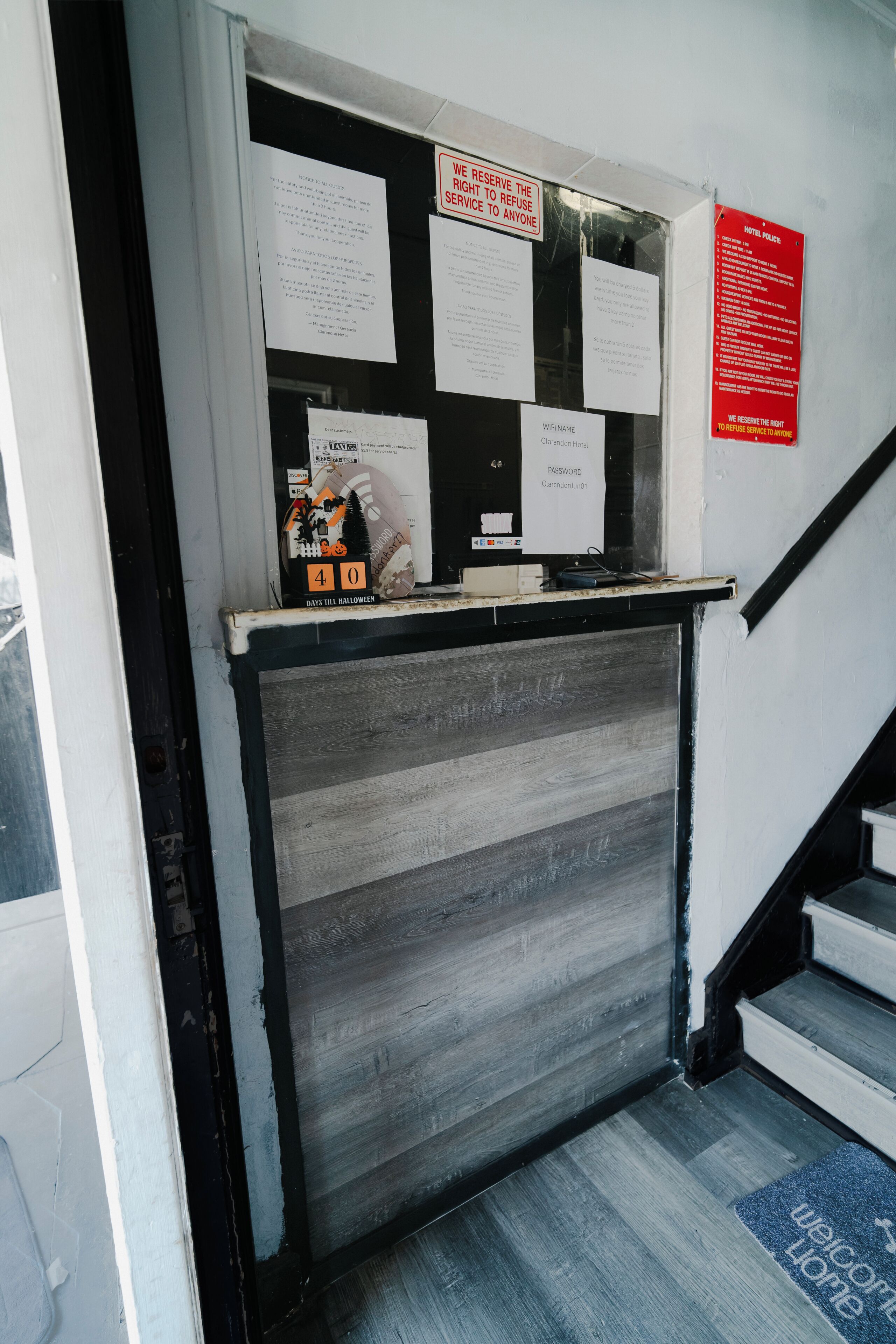 Un comptoir d’accueil d’hôtel avec divers avis affichés et un panneau indiquant le mot de passe du réseau Wi-Fi.