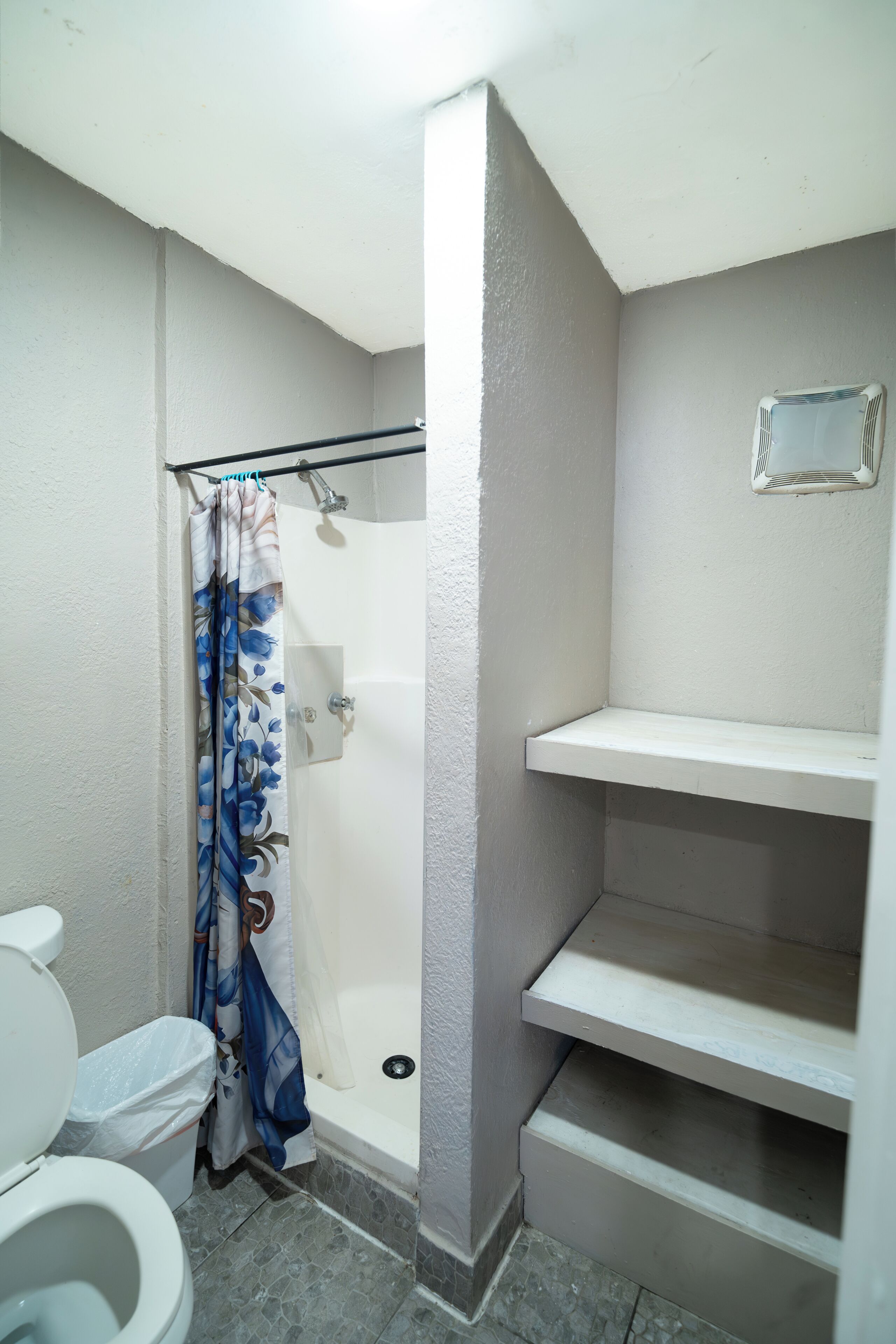 A bathroom with a toilet, shower, and a shelf unit.