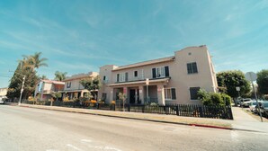 A two-story building with a flat roof, a visible address number, and a black metal fence in front. - Clarendon Hotel (Huntington Park)