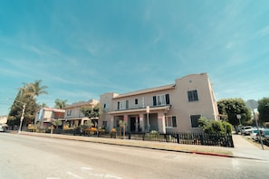 Un edificio de dos pisos con techo plano, un número de dirección visible y una cerca metálica negra al frente.