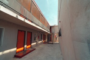 A narrow alleyway with a building featuring a red door and a staircase leading to an upper level. - Clarendon Hotel (Huntington Park)