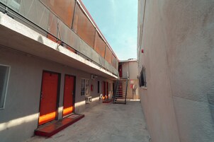 Un callejón estrecho con un edificio que tiene una puerta roja y una escalera que sube a un nivel superior.
