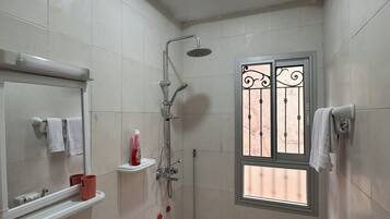 Casa de banho com chuveiro, pia, sanita e janela com grades decorativas.