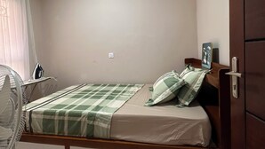 Um quarto com uma cama, mesa de cabeceira, ventilador e armário.