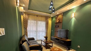 Uma sala de estar com sofá, poltronas, mesa de centro, televisão e uma parede decorativa.
