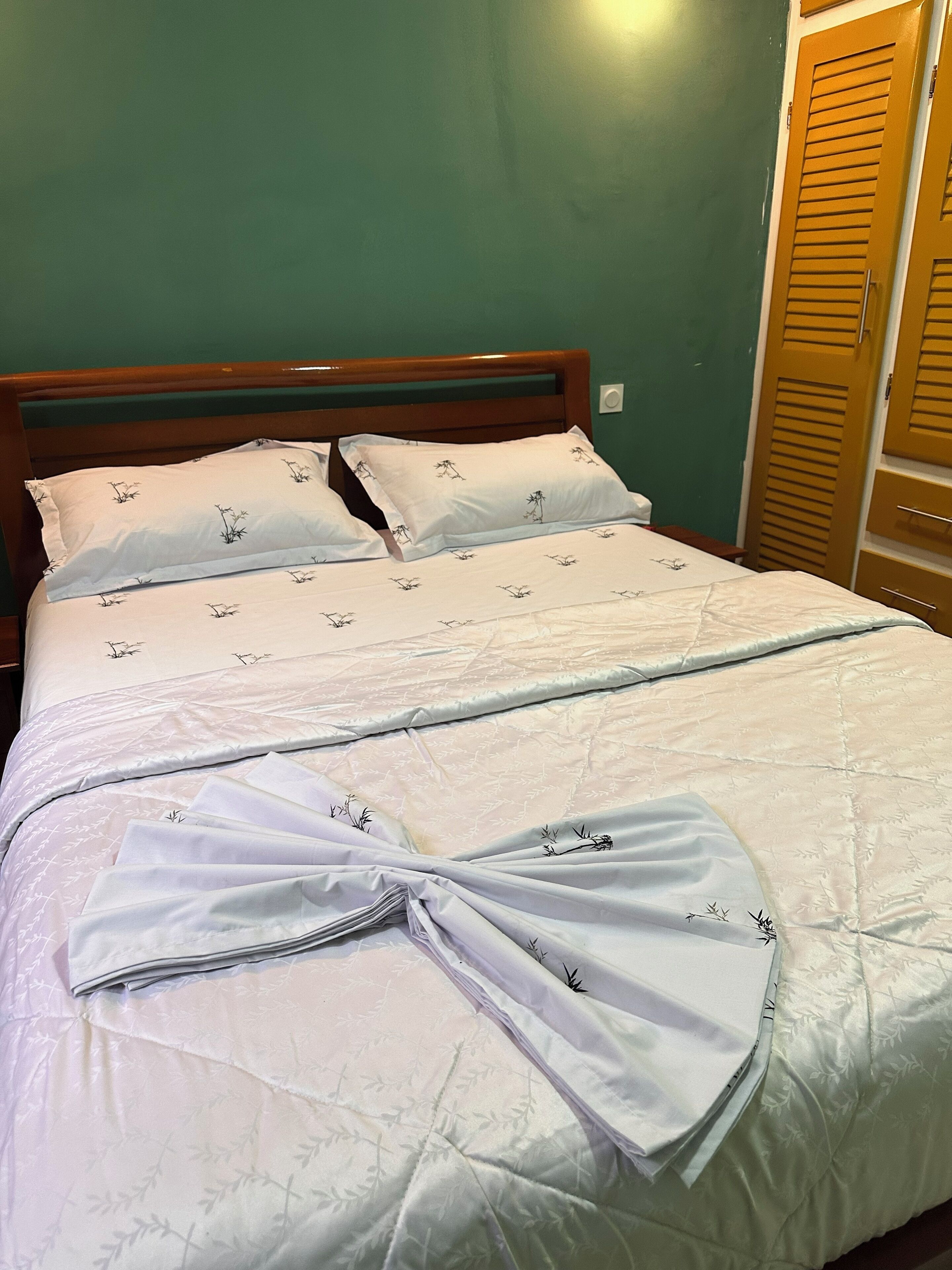 Una cama bien hecha con sábanas blancas y un lazo decorativo, cabecera de madera y pared verde.