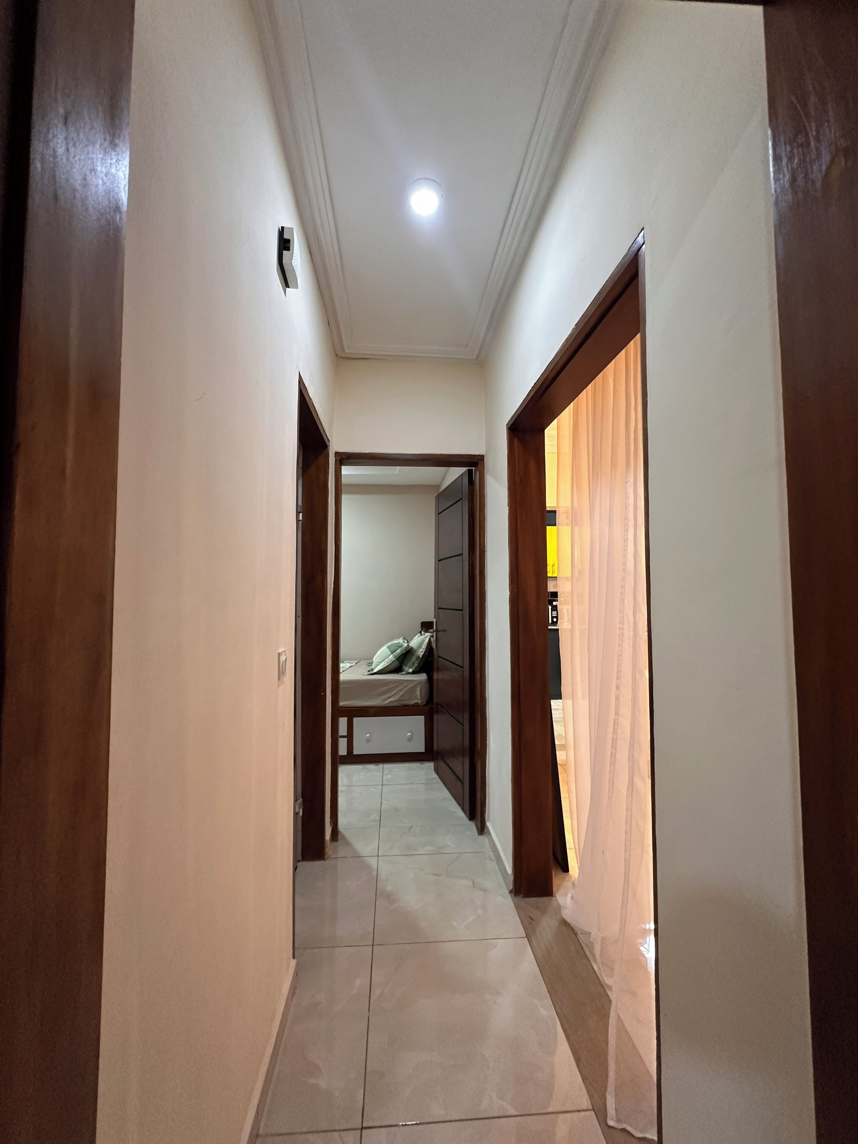 A hallway with a bed in the background, a ceiling light, and a door on the right.