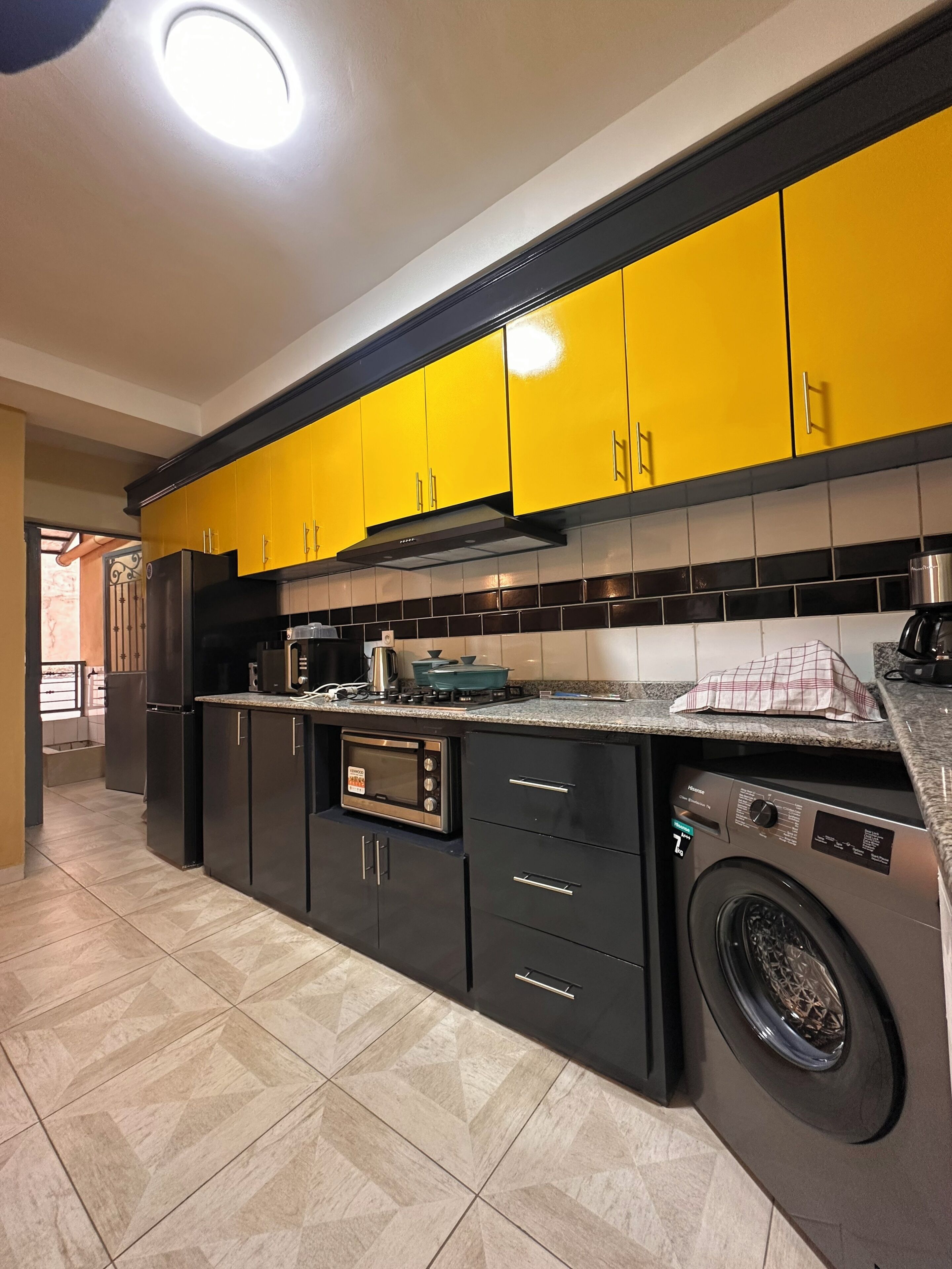 A kitchen with yellow cabinets, a built-in oven, a microwave, and a washing machine.