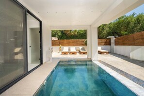 A modern outdoor swimming pool with a wooden deck and lounge chairs. - Villa Maria Sostis by Villa Plus (Agios Sostis)