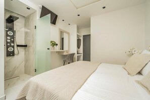 A modern bedroom with a large bed, a shower area, a vanity, and a television mounted on the wall. - Villa Maria Sostis by Villa Plus (Agios Sostis)