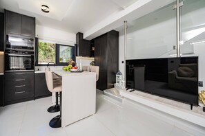 Eine moderne Küche mit dunklen Schränken, einem Essbereich mit einem weißen Tisch und einem großen Fenster.