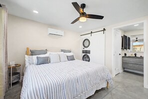 Quarto com cama, ventilador de teto, ar condicionado, máquina de lavar e banheiro com pia e espelho.